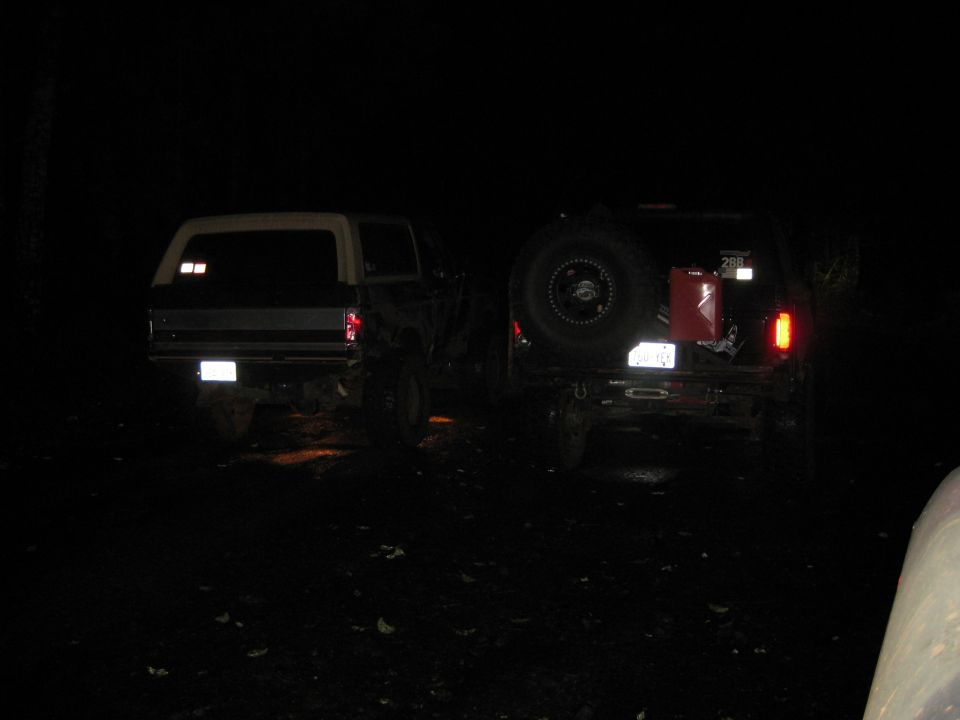 Two SUVs parked at night, one with a spare tire and gas can mounted on the rear. The one on the left appears to be a 1978 Ford Bronco