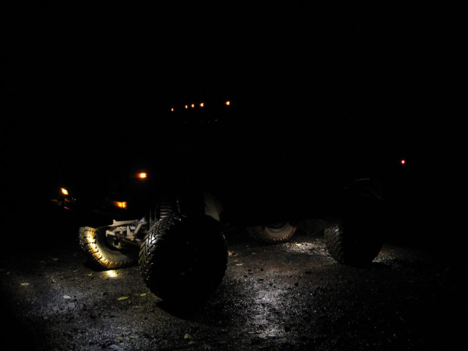 off-road vehicle with large tires parked on wet ground at night, headlights on