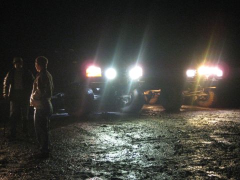 1979 Ford Bronco - Two 1979 Ford Broncos are parked at night, their headlights illuminating the muddy ground.