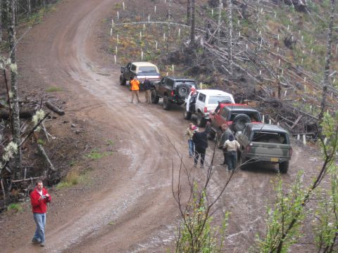 1979 Ford Bronco - A group of off-road vehicles are stopped on a dirt track, with people milling around.
