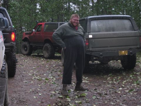 1979 Ford Bronco - Man poses between two SUVs parked on a dirt path in a wooded area.