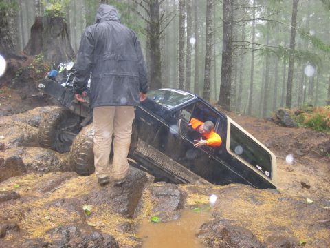 1979 Ford Bronco - Two people are near a vehicle that is stuck in the mud in a wooded area.