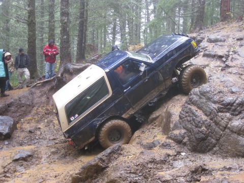 1979 Ford Bronco - A vehicle attempts to traverse a difficult, muddy, and rocky off-road course with spectators observing.
