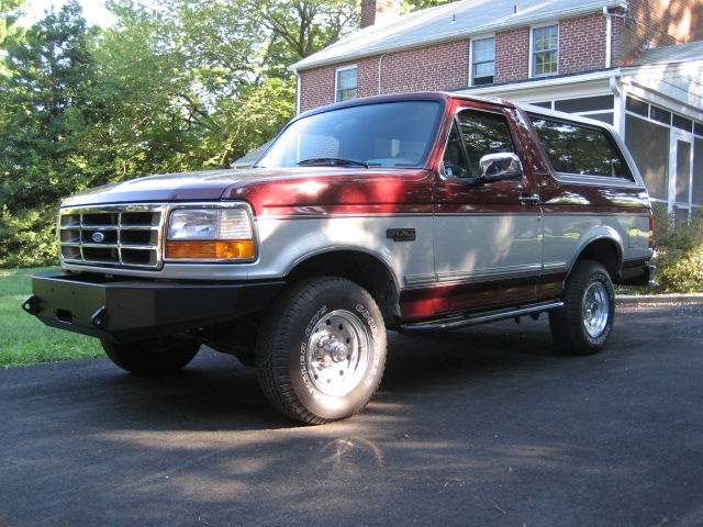Red and silver 1996 Ford Bronco with aftermarket bumper parked on asphalt driveway
