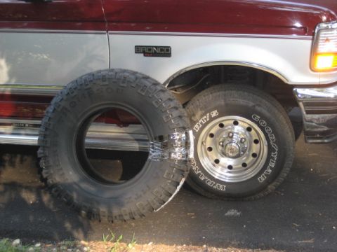 1996 Ford Bronco - A 1996 Ford Bronco is shown with a spare tire placed in front of its wheel.