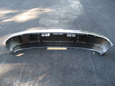 1996 Ford Bronco - A detached front bumper sits on asphalt, showing its internal mounting structure and chrome trim.