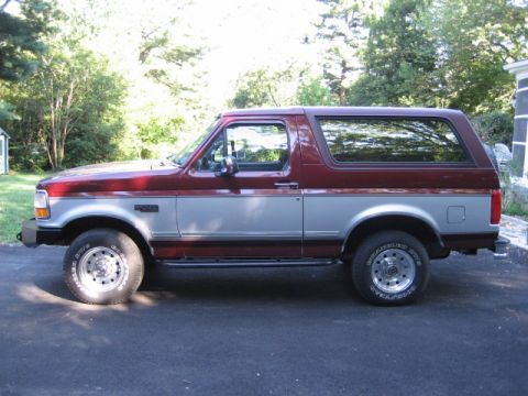 1996 Ford Bronco - This two-tone Ford Bronco is seen from the side, parked on a paved surface with trees in the background.