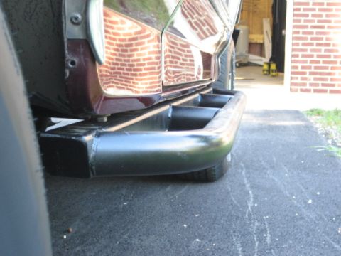 1996 Ford Bronco - Close-up view of the rear bumper and side panel of a dark red SUV with aftermarket black tubular steps.