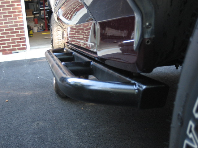 Close-up of a black aftermarket tubular rear bumper guard installed on a dark red vehicle