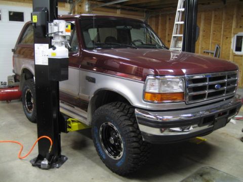 1996 Ford Bronco - Maroon and silver Ford Bronco is raised on a car lift inside a garage.