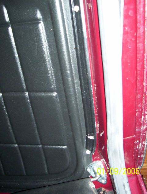 1979 Ford Bronco - A close-up view of the interior door panel and frame of a vehicle, showing black quilted upholstery and red exterior paint.
