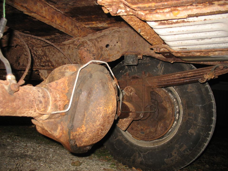 Rust-covered rear axle, differential, and leaf spring under a truck bed