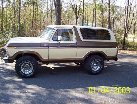 1979 Ford Bronco - A two-tone beige and brown Ford Bronco is parked outdoors on an asphalt surface with trees in the background.