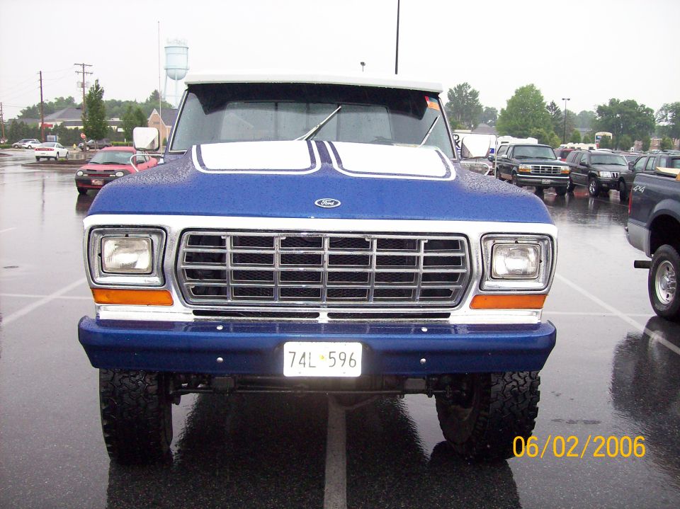Blue and white 1970s Ford truck front view with chrome grille on a wet parking lot