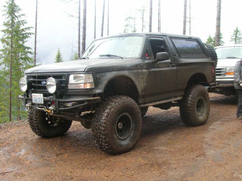 1996 Ford Bronco - Modified 1996 Ford Bronco on a forest road, with another vehicle nearby.