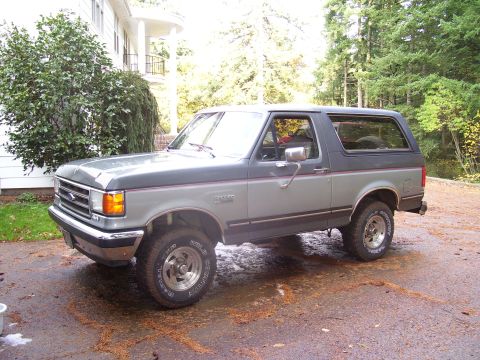 1991 Ford Bronco - Two-tone gray 1991 Ford Bronco with red pinstripes sits outside.