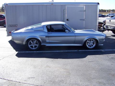 2001 Ford Crown Victoria - A classic silver Ford Mustang Fastback is parked beside a large silver trailer.