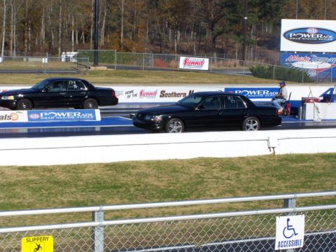 2001 Ford Crown Victoria - Two black sedans, appearing to be 2001 Ford Crown Victorias, compete on a drag racing track.
