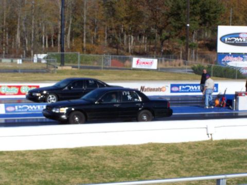 2001 Ford Crown Victoria - Two black sedans prepare for a drag race on a sunny day.