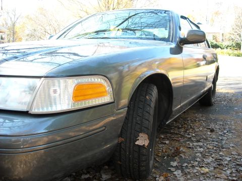 2000 Ford Crown Victoria - A gray 2000 Ford Crown Victoria is viewed from the front quarter, showing its headlight and fender.
