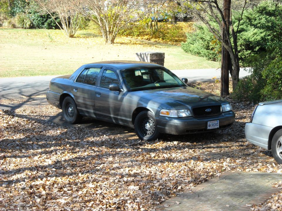 Dark gray 2000 Ford Crown Victoria parked on a leaf-covered driveway, front quarter view