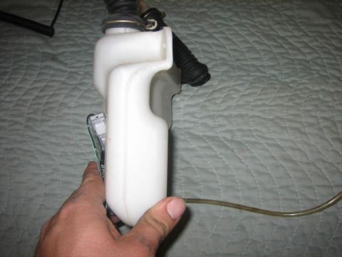 1996 Ford Thunderbird - A white plastic windshield washer fluid reservoir is shown from the side, held by a person's hand.