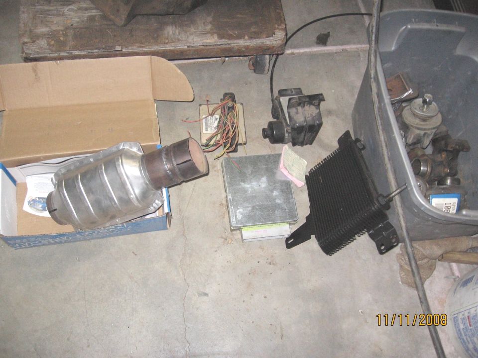 Used catalytic converter, ECU, oil cooler, mount and wiring pigtail laid out on a garage floor