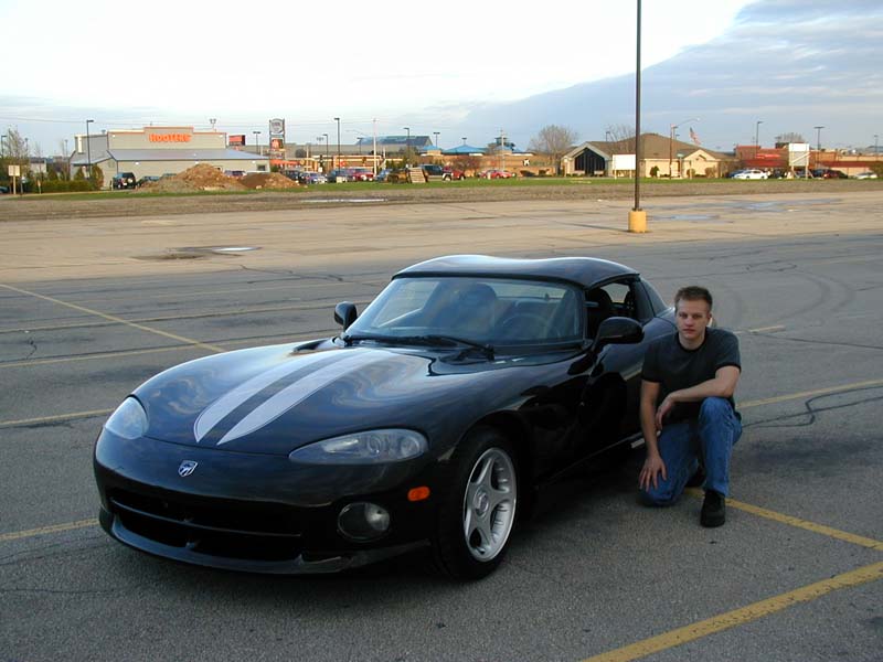Black Dodge Viper with silver stripes and man crouching beside it in a parking lot