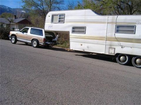 2000 Mercury Grand Marquis - A tan and white SUV is seen from the side, towing a large white trailer on a paved road.