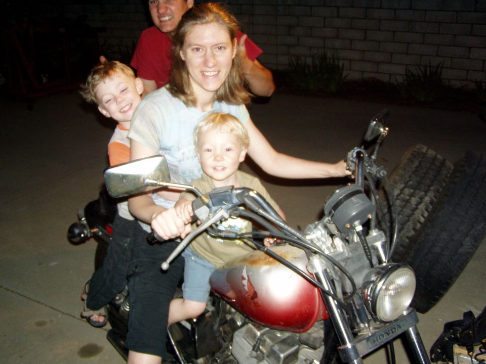 Woman and two young boys sitting on a red motorcycle at night