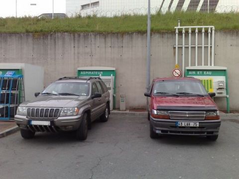 1991 Ford Crown Victoria - Two SUVs, a Jeep Grand Cherokee and a red minivan, are parked at a service station with air and water dispensers.