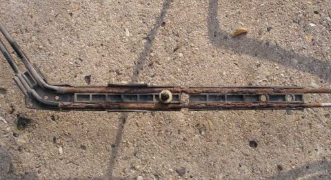 1997 Ford Taurus - A removed seat track assembly laid on a concrete driveway, its steel rails heavily surface-rusted with a brass-colored pivot bolt at the ce…