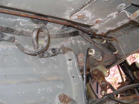 1997 Ford Taurus - Underside view of a car's floorpan and rear subframe showing a heavily rusted steel brake line running along the body seam, joined by a coi…