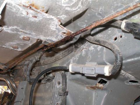 1997 Ford Taurus - Underbody view of a vehicle showing a heavily rusted steel brake or fuel line running diagonally across gray sheet metal, with a white two-…