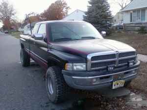 1996 Dodge 1500 - A dark colored Dodge Ram pickup truck is parked on the side of a street in a residential area. The front of the vehicle is visible.
