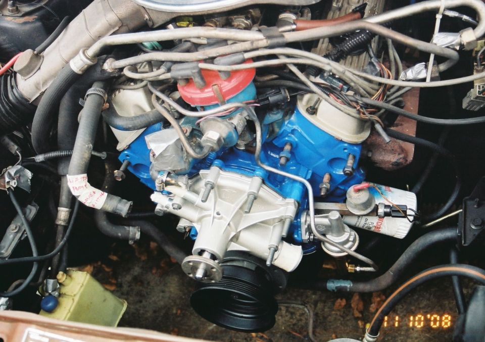 Engine bay detail showing blue painted intake manifold, water pump, distributor cap, and oil filter