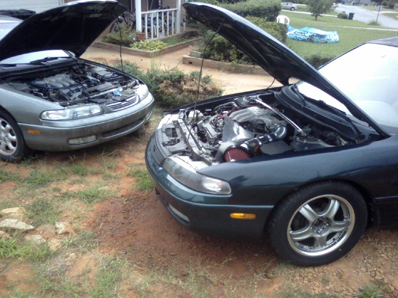 Two sedans with hoods open parked on grass, engine work