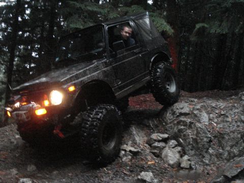 1986 Ford Bronco - Off-road vehicle navigating a challenging rocky path in a wooded area.
