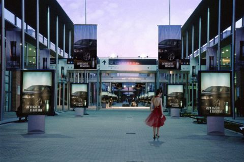 2003 Mercury Marauder - A woman in a red dress walks through a plaza displaying advertisements for Armani Mania, which feature a dark sedan.