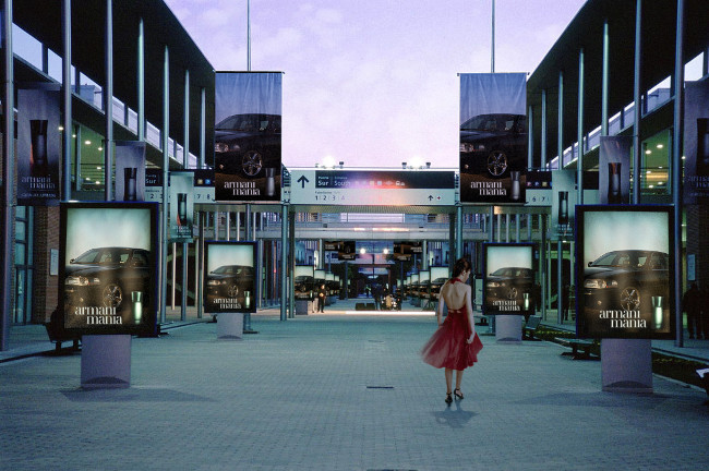 Twilight mall promenade with armani mania ad light boxes and a woman in a red dress walking away