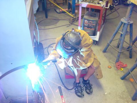 1948 Jeep Wrangler - A person in protective gear welds a car's body panel in a workshop setting.