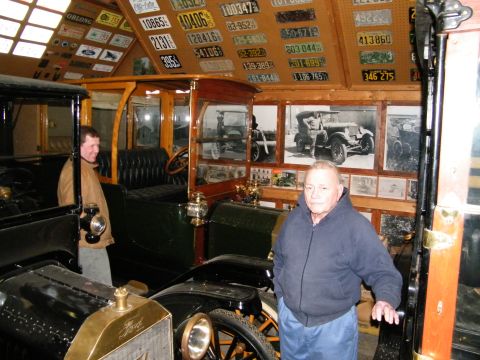 1909 Ford Model T - A collection of antique vehicles and numerous license plates are displayed indoors.