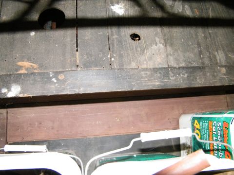 1909 Ford Model T - A close-up view of weathered wooden floorboards with a hole and a box of cat litter.