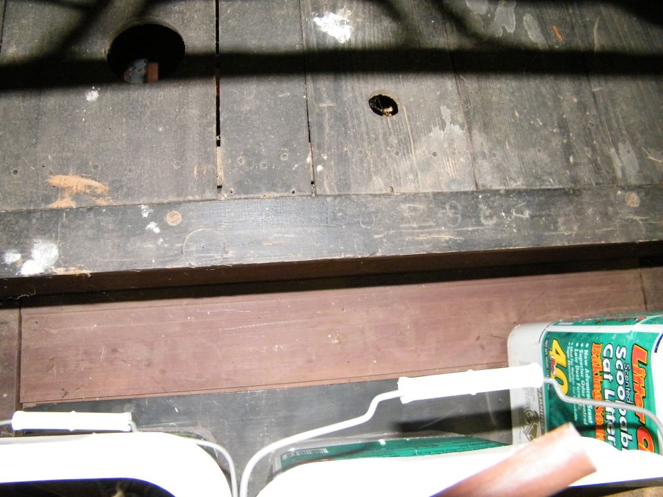Wooden floorboards with a hole, a white wire, and a green box of cat litter