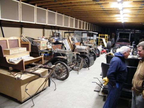 1909 Ford Model T - A collection of antique automobiles are stored indoors, with two men observing the vehicles.