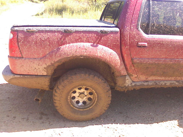 Mud-covered red 2001 Ford Explorer pickup truck, side view showing rear wheel and bed cover