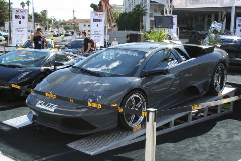 1998 Ford Crown Victoria - A dark gray Lamborghini Murciélago is displayed on ramps with other cars in the background.