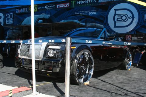 1998 Ford Crown Victoria - A heavily modified Chrysler 300C with prominent DUB branding and oversized chrome wheels is displayed under a tent.
