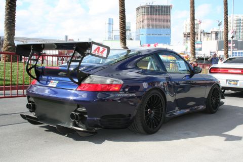 1998 Ford Crown Victoria - A dark blue Porsche 911 with a prominent rear wing and aggressive body kit is parked next to another vehicle.