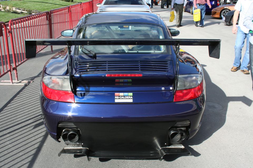 Rear view of a blue Porsche 911 GT3 RS with a large rear wing and dual exhaust pipes. RS-CALDERA sticker on the trunk